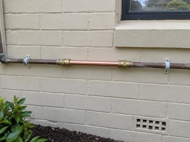 Repaired copper water pipe on a painted brick exterior wall beside a window in Tingira Heights