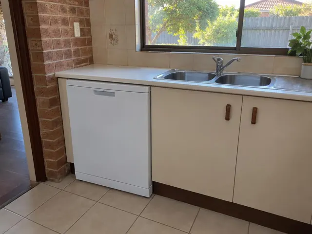 White dishwasher under a kitchen bench beside a double sink and tiled splashback in Belmont North
