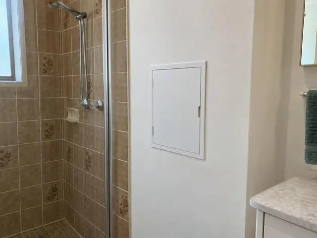 Bathroom shower wall with a small access panel beside tiled shower in a home interior in Jewells
